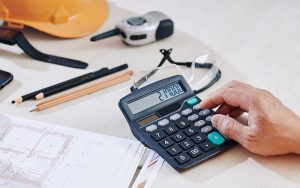 hand using calculator on desk with construction items