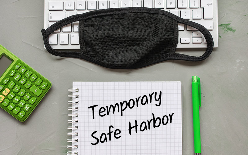 Keyboard with a mask on top of it with a notebook that says "Temporary Safe Harbor"